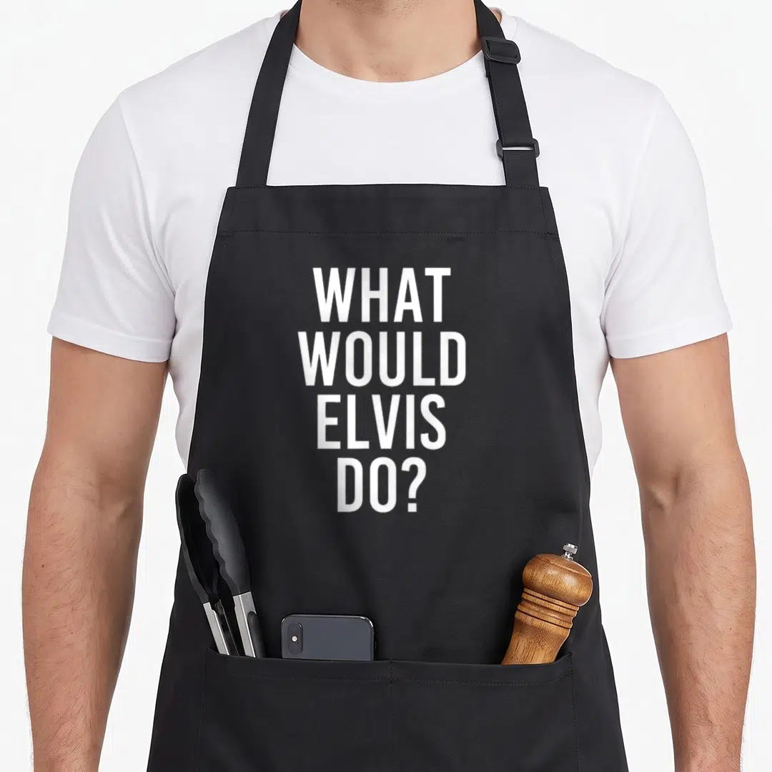 Would joke apron - White stacked text reading WHAT WOULD ELVIS DO? on grey fabric — shown on a black cotton canvas apron against a white background