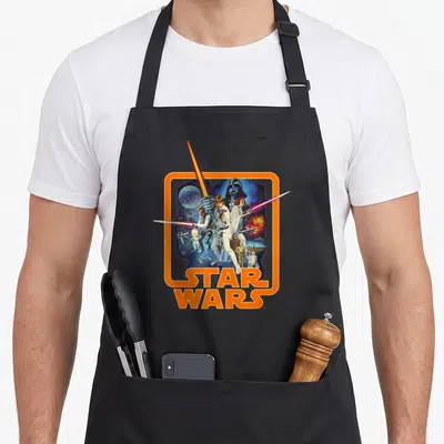 Hope badger apron - Star Wars photo collage with Luke Skywalker inside orange rounded frame and bold orange lettering — shown on a black cotton canvas apron against a white background
