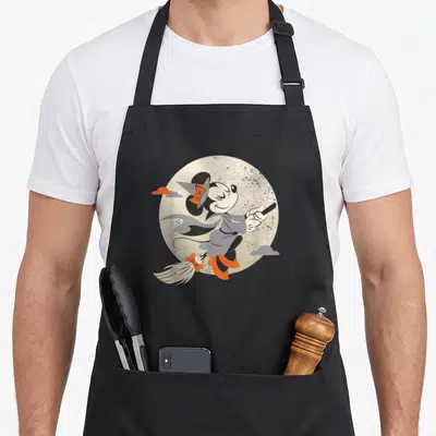 Witch flying apron - Cartoon Minnie Mouse in grey robes riding a broom across a moon with orange and grey clouds — shown on a black cotton canvas apron against a white background
