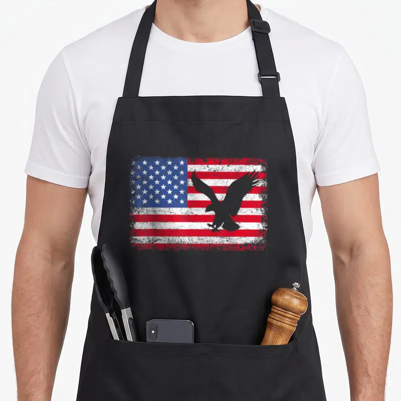 Patriotic eagle 4th of july apron - Grey eagle silhouette over distressed red white and blue American flag pattern — shown on a black cotton canvas apron against a white background