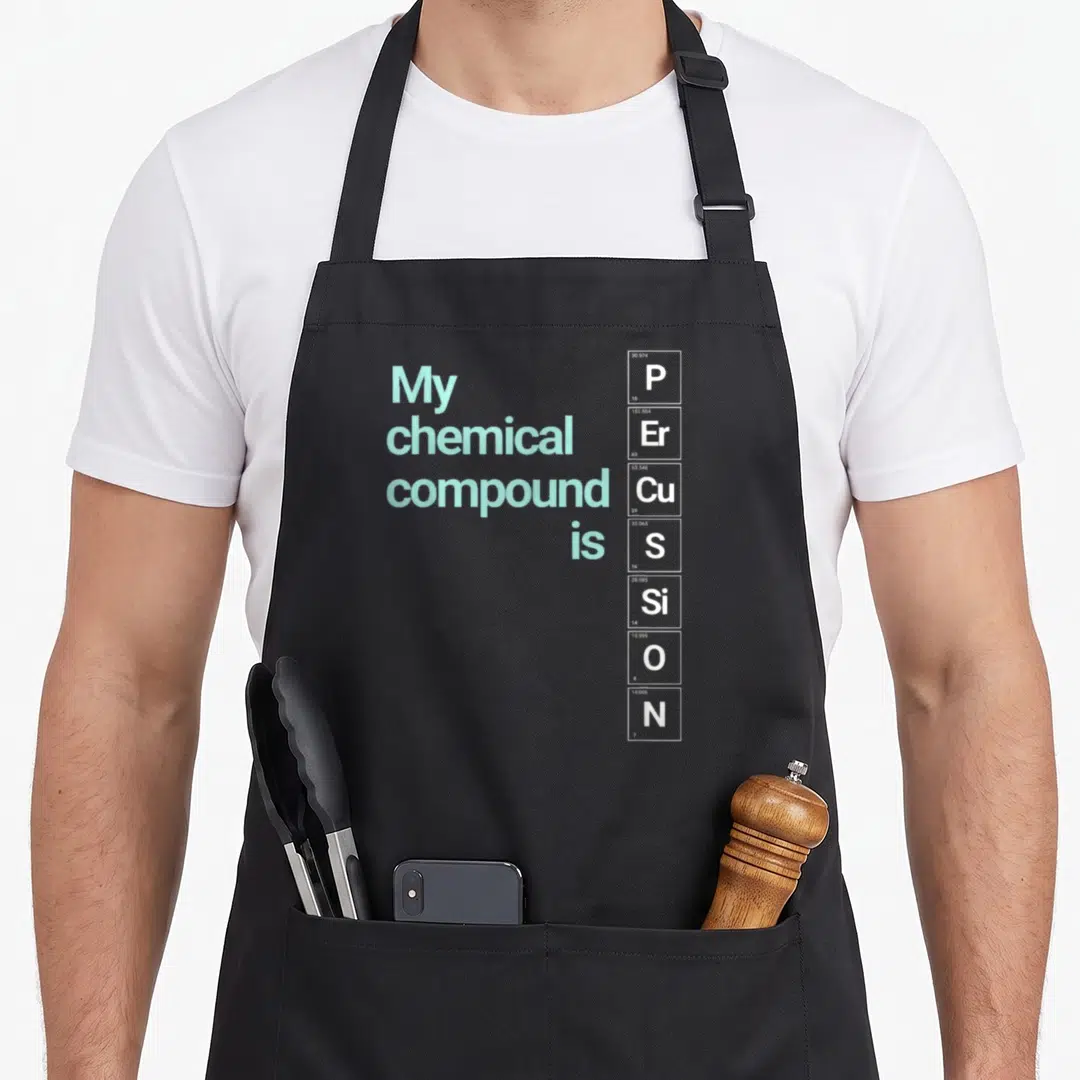 Percussion geek apron - Periodic table elements P Er Cu S Si O N spelling percussion next to light green text — shown on a black cotton canvas apron against a white background