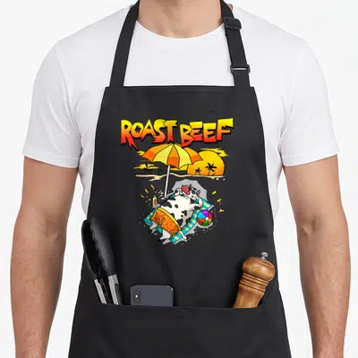 Roast cow apron - Cartoon cow sunbathing on beach towel under umbrella with ROAST BEEF text — shown on a black cotton canvas apron against a white background