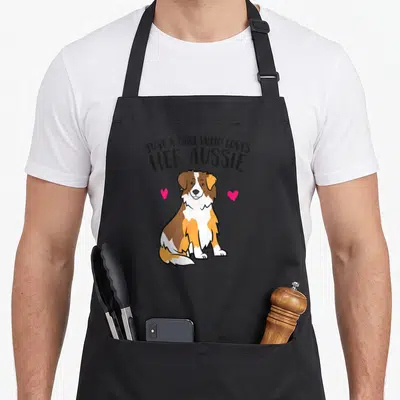 Shepherd aussie australian apron - Cartoon Australian Shepherd dog with arched text and two pink hearts on left — shown on a black cotton canvas apron against a white background