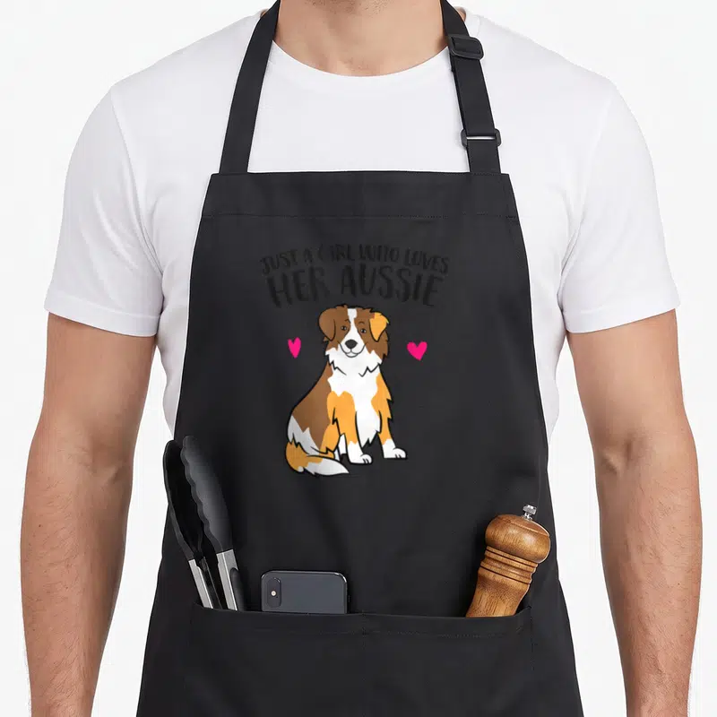 Shepherd aussie australian apron - Cartoon Australian Shepherd dog with arched text and two pink hearts on left — shown on a black cotton canvas apron against a white background