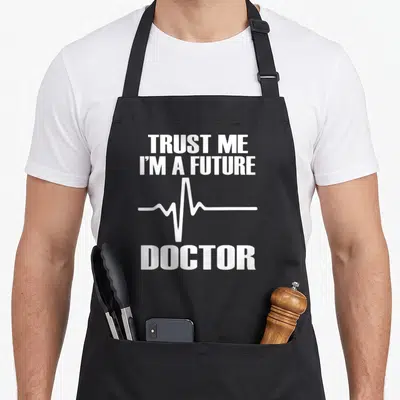 Future medical doctor apron - White stacked text reading Trust Me I'm A Future Doctor with EKG line graphic — shown on a black cotton canvas apron against a white background