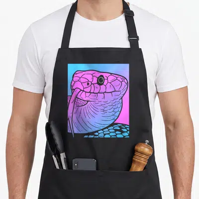 Snake goth apron - Cartoon snake head in pink and purple scales against a blue and pink gradient background — shown on a black cotton canvas apron against a white background