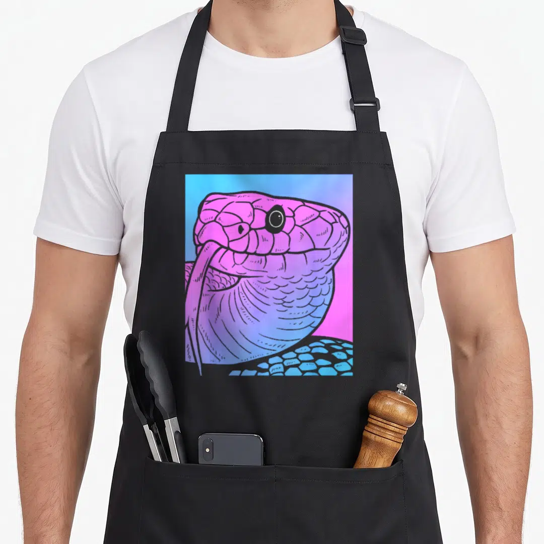 Snake goth apron - Cartoon snake head in pink and purple scales against a blue and pink gradient background — shown on a black cotton canvas apron against a white background