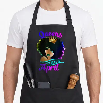 April pisce birthday apron - Crowned woman illustration with Queens Are Born In April text in blue pink and gold — shown on a black cotton canvas apron against a white background