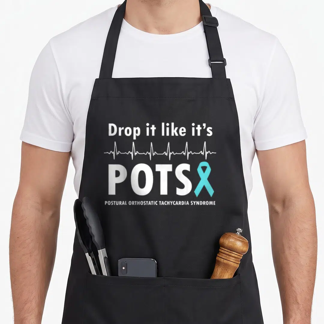 Drop pot apron - White text Drop it like it's POTS with blue ribbon and heartbeat line on black fabric — shown on a black cotton canvas apron against a white background