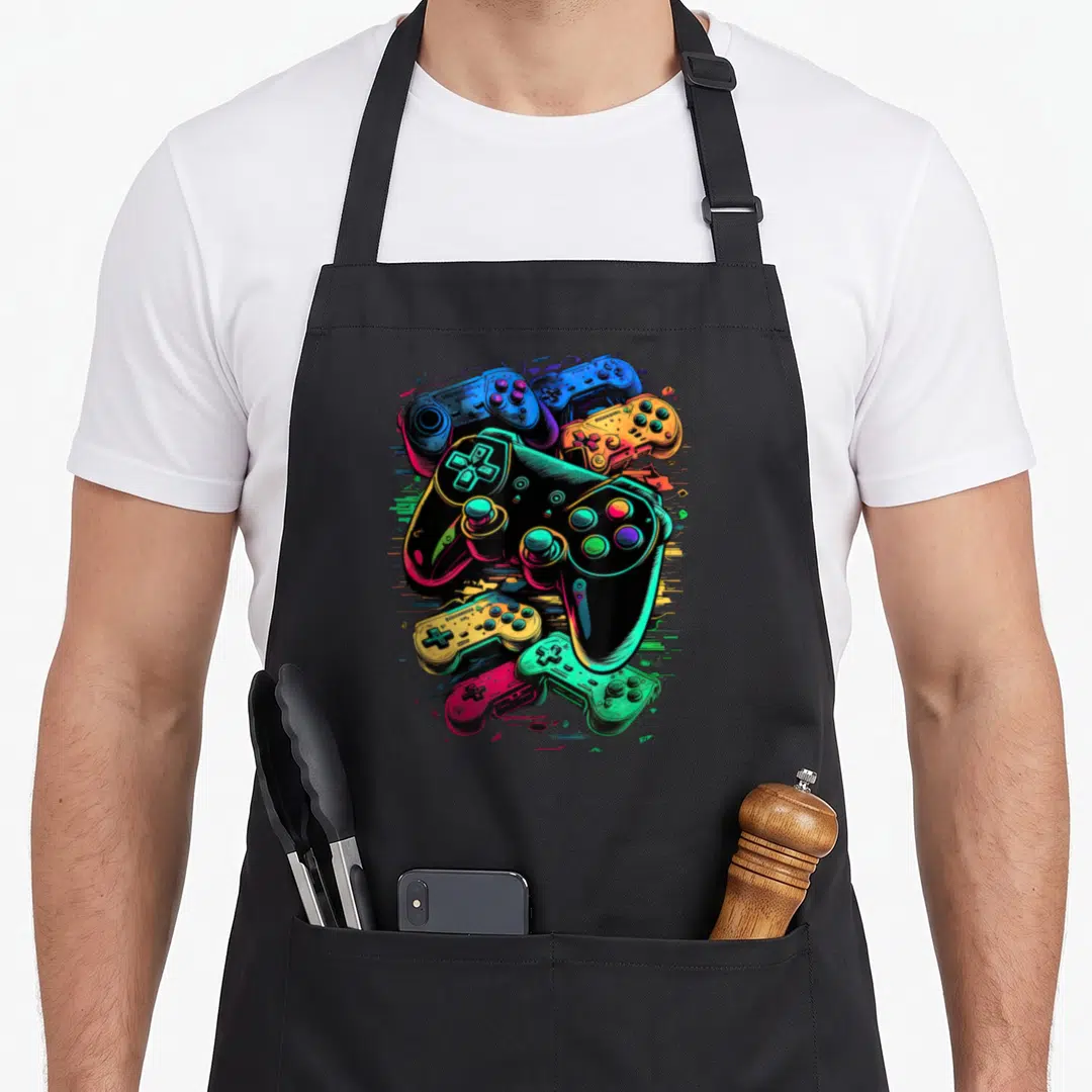 Control gamer video game apron - Six overlapping cartoon game controllers in neon green, pink, blue, yellow, and black — shown on a black cotton canvas apron against a white background