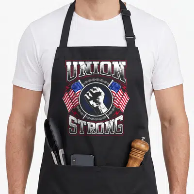 Union pro apron - Distressed UNION STRONG text surrounding a fist, two flags, and chain with lightning bolts — shown on a black cotton canvas apron against a white background