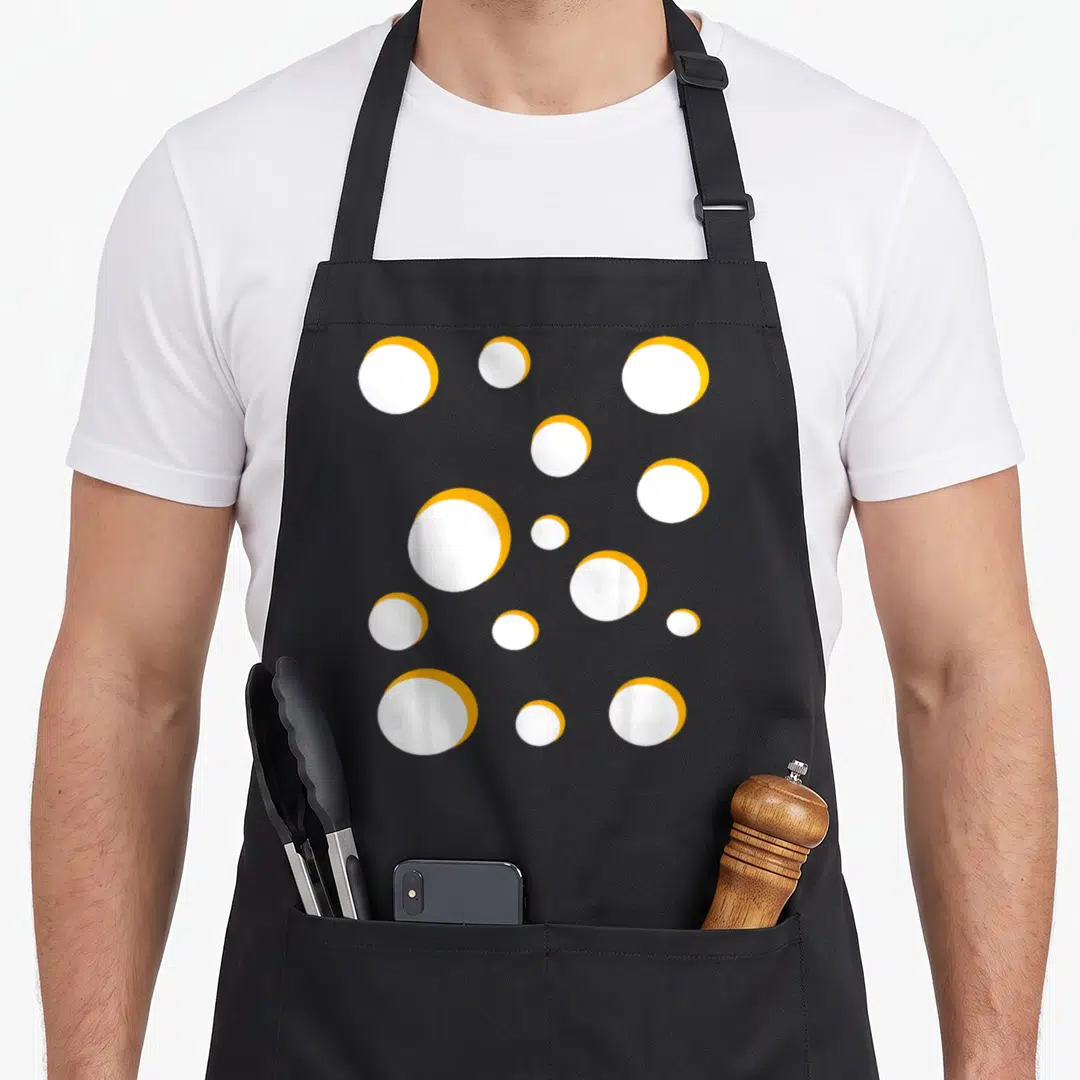 Gouda swiss apron - Scattered white circles with orange rims representing cheese holes — shown on a black cotton canvas apron against a white background