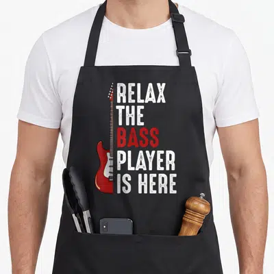 Relax bass apron - Red electric bass guitar next to stacked white and red distressed text — shown on a black cotton canvas apron against a white background
