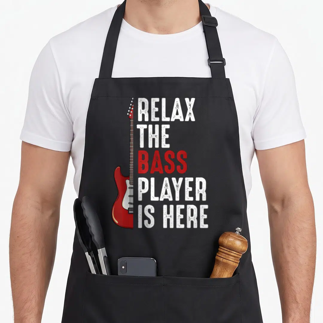 Relax bass apron - Red electric bass guitar next to stacked white and red distressed text — shown on a black cotton canvas apron against a white background