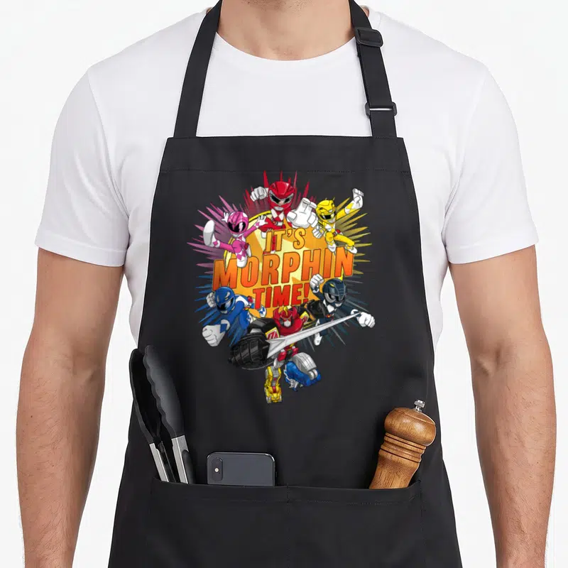 Morphin rangers apron - Five Power Rangers in red yellow pink blue black surrounding stacked IT'S MORPHIN TIME! text — shown on a black cotton canvas apron against a white background