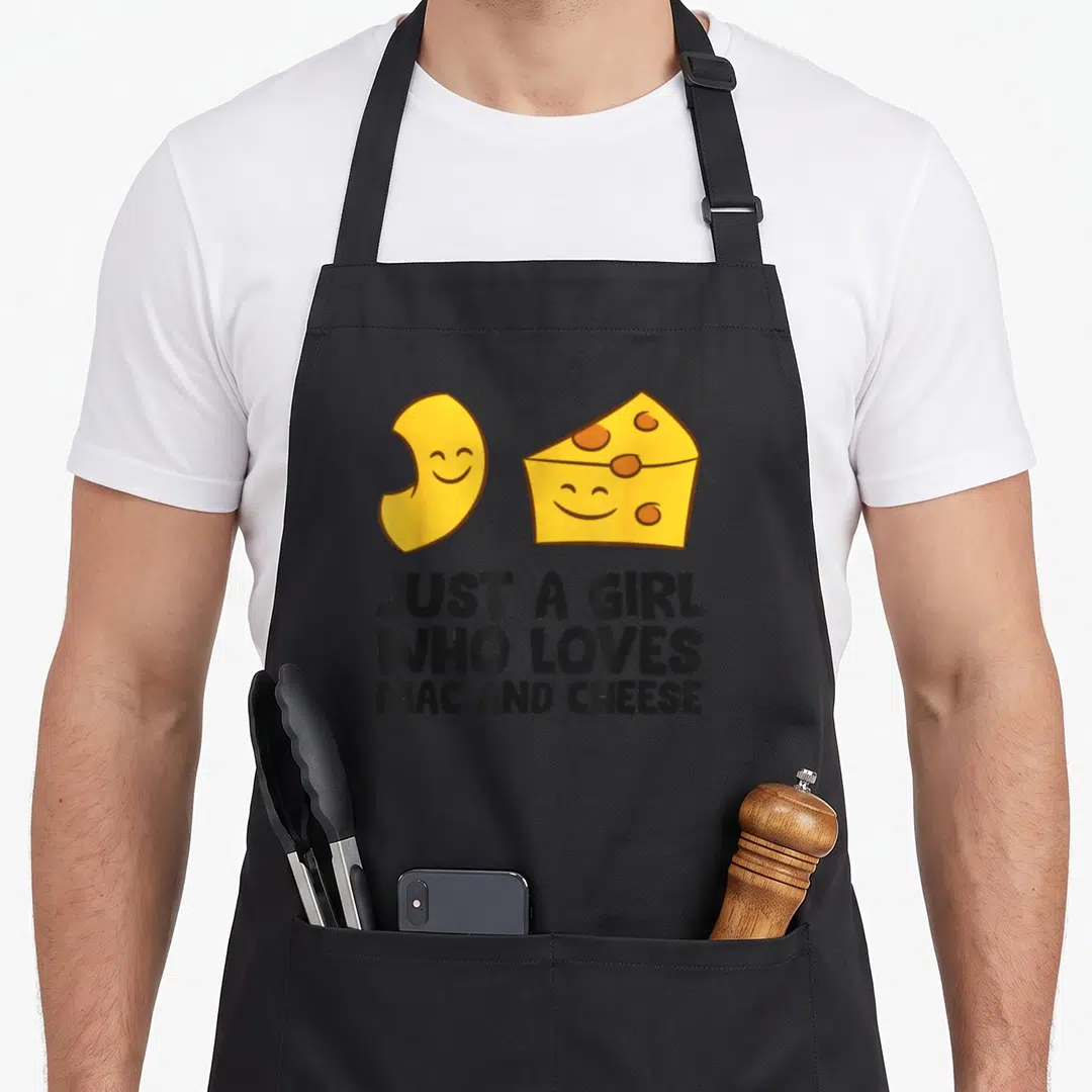 Cute macaroni mac apron - Smiling yellow cheese wedge and macaroni noodle above black text — shown on a black cotton canvas apron against a white background