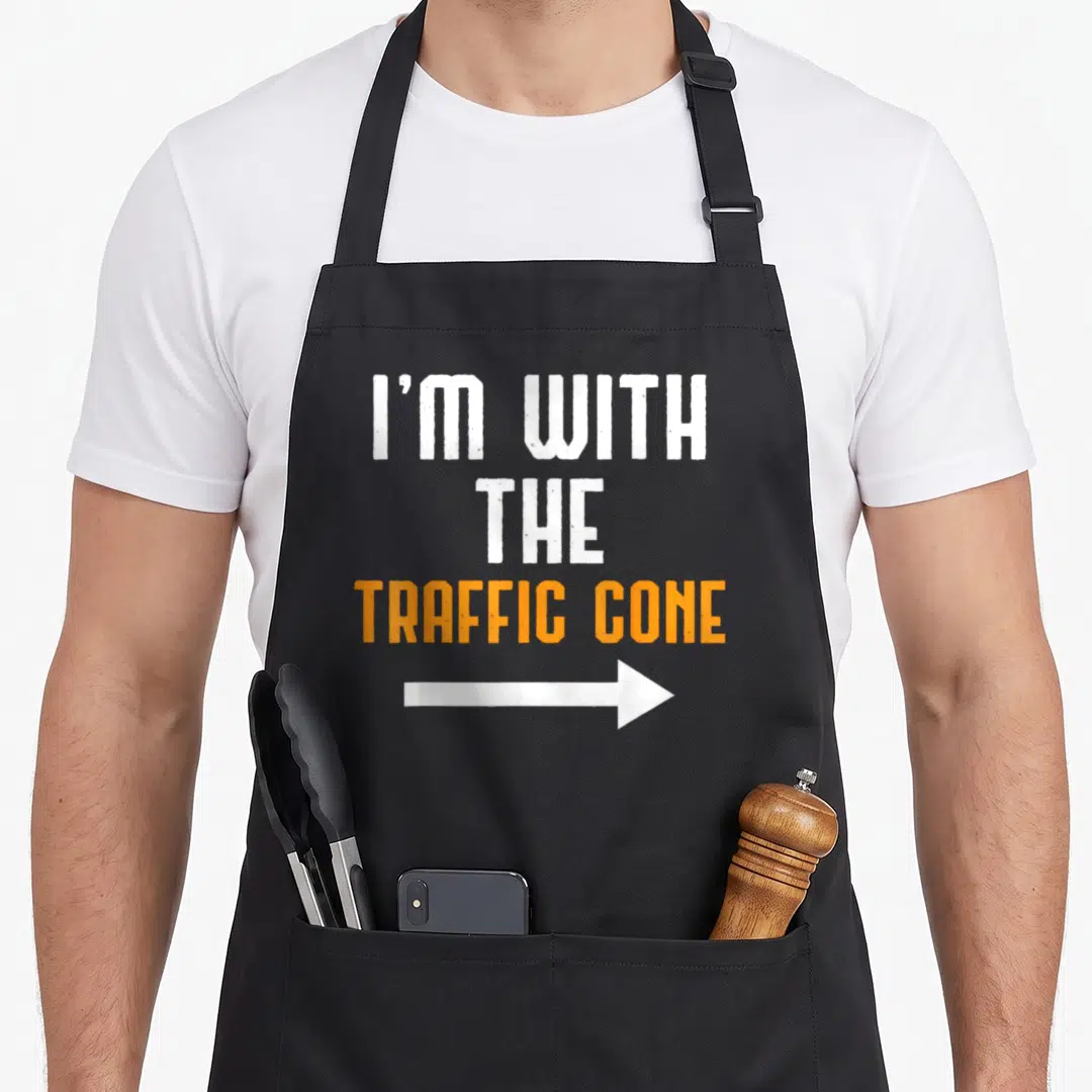 Traffic couple apron - I'M WITH THE TRAFFIC CONE text and white arrow in distressed white and orange — shown on a black cotton canvas apron against a white background