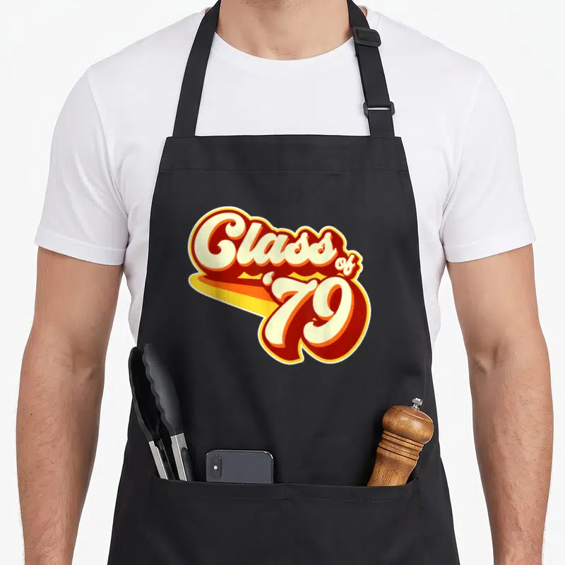 Reunion 40th apron - Stacked cream red and orange Class of 79 retro typography design — shown on a black cotton canvas apron against a white background