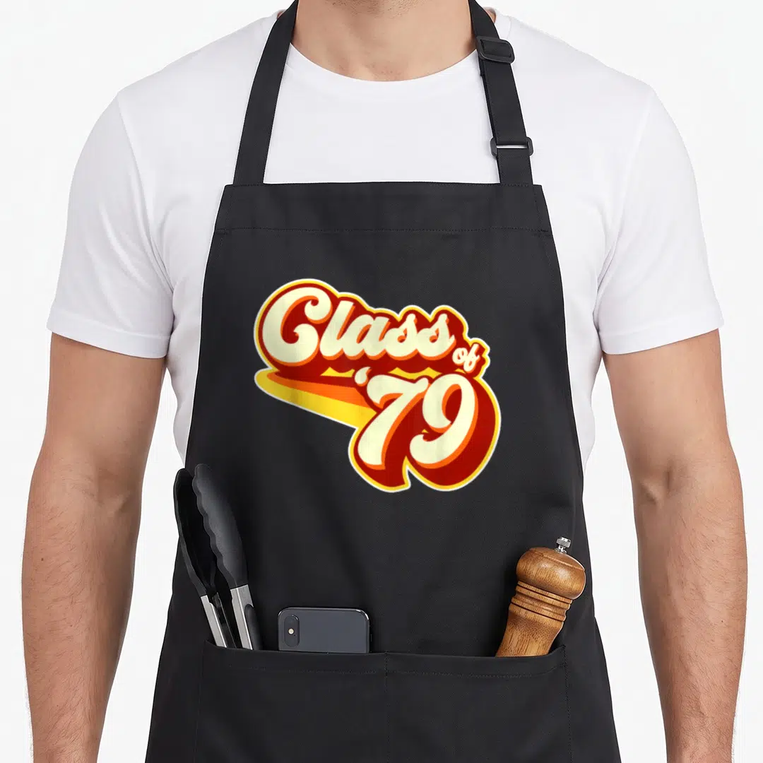 Reunion 40th apron - Stacked cream red and orange Class of 79 retro typography design — shown on a black cotton canvas apron against a white background