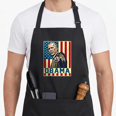 Barack novelty apron - Retro portrait of Obama pointing forward over USA flag with blue OBAMA text bar — shown on a black cotton canvas apron against a white background