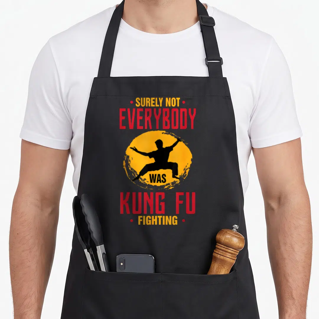 Certainly joke apron - Stacked red and yellow text around black martial artist silhouette in yellow circle — shown on a black cotton canvas apron against a white background