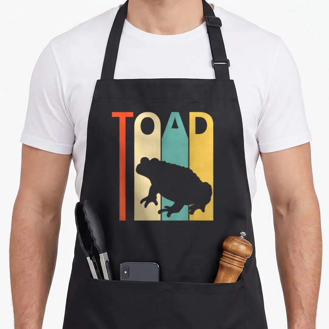Cute toad apron - TOAD text in red cream teal yellow stripes with grey toad silhouette overlay — shown on a black cotton canvas apron against a white background