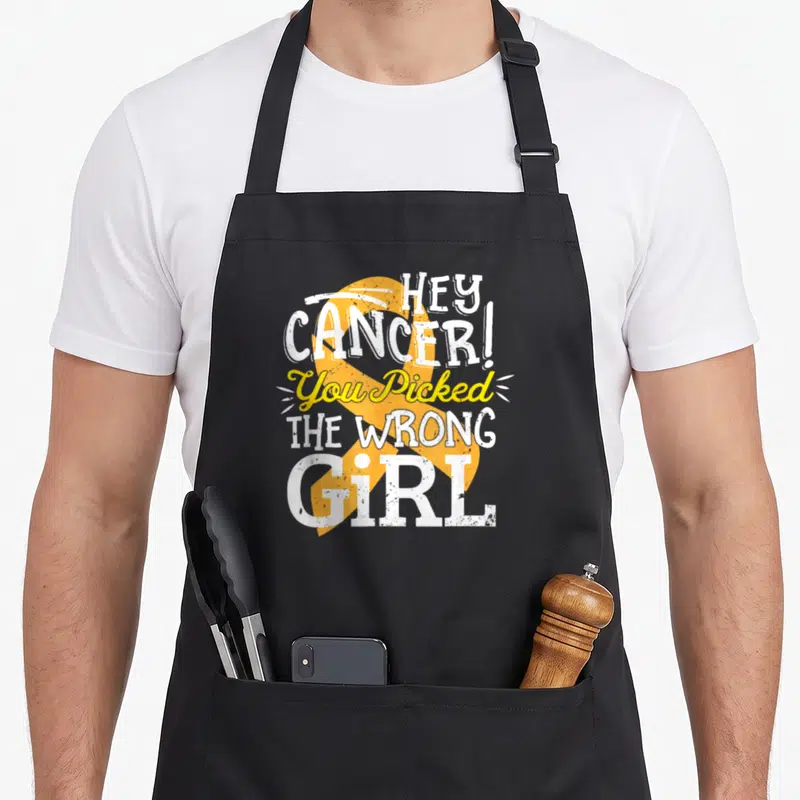 Childhood crab legs apron - Distressed white and yellow text reading HEY CANCER! You Picked THE WRONG GiRL over a large — shown on a black cotton canvas apron against a white background
