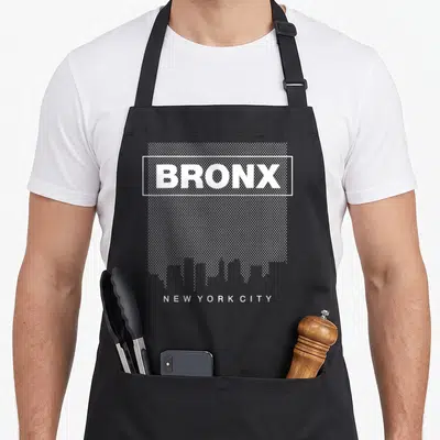 Bronx new york apron for women - White BRONX text in rectangle over dots with skyline and NEW YORK CITY below — shown on a black cotton canvas apron against a white background