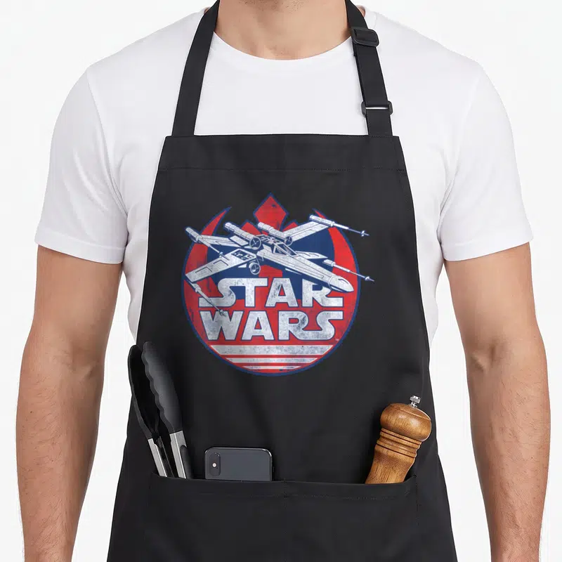 Symbol x apron - Distressed spaceship over red blue circle with white Star Wars text — shown on a black cotton canvas apron against a white background
