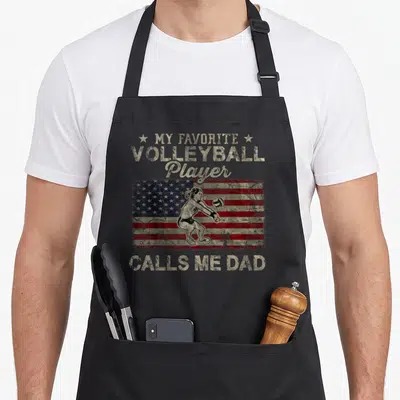 Player volleyball dad apron - My Favorite Volleyball Player Calls Me Dad text over distressed USA flag and athlete — shown on a black cotton canvas apron against a white background