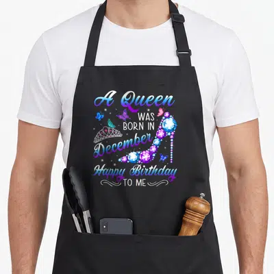 Retro queen birthday apron - Gem covered high heel shoe with crown, butterflies, and December birthday text in blue — shown on a black cotton canvas apron against a white background