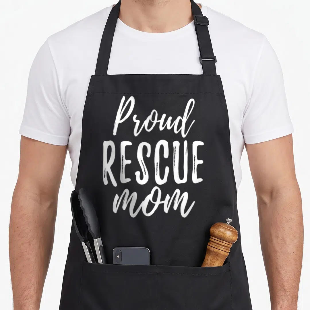 Animal grill rescue apron - White stacked text Proud RESCUE mom on black bib apron, no images — shown on a black cotton canvas apron against a white background