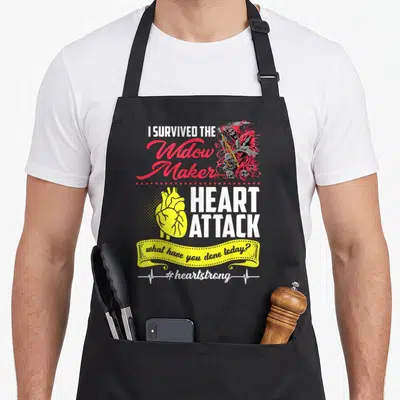 Survived maker apron - I Survived Widow Maker Heart Attack text with Grim Reaper and yellow anatomical heart graphic — shown on a black cotton canvas apron against a white background