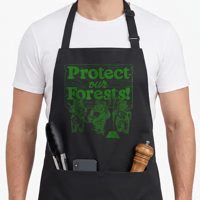 Protect wars new apron - Three Ewoks standing below stacked text Protect our Forests! in green retro style — shown on a black cotton canvas apron against a white background