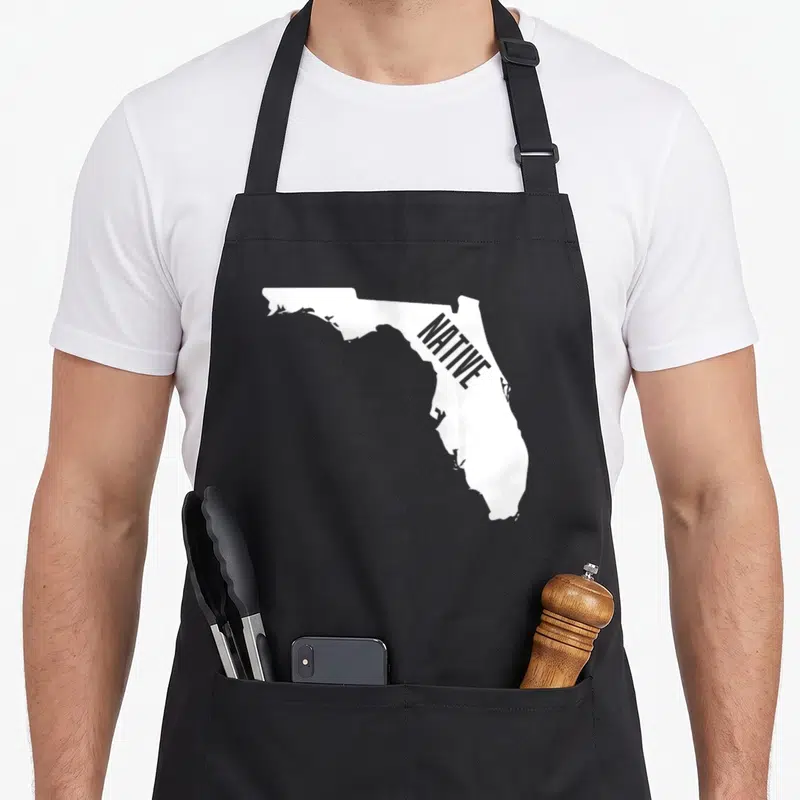 Native outline of an apron - White Florida map silhouette with grey diagonal NATIVE text on dark background — shown on a black cotton canvas apron against a white background