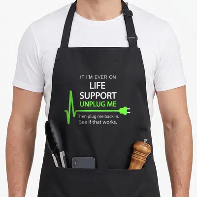 Support geek apron - White and lime green text reading If I'm Ever On Life Support Unplug Me with a plug graphic — shown on a black cotton canvas apron against a white background