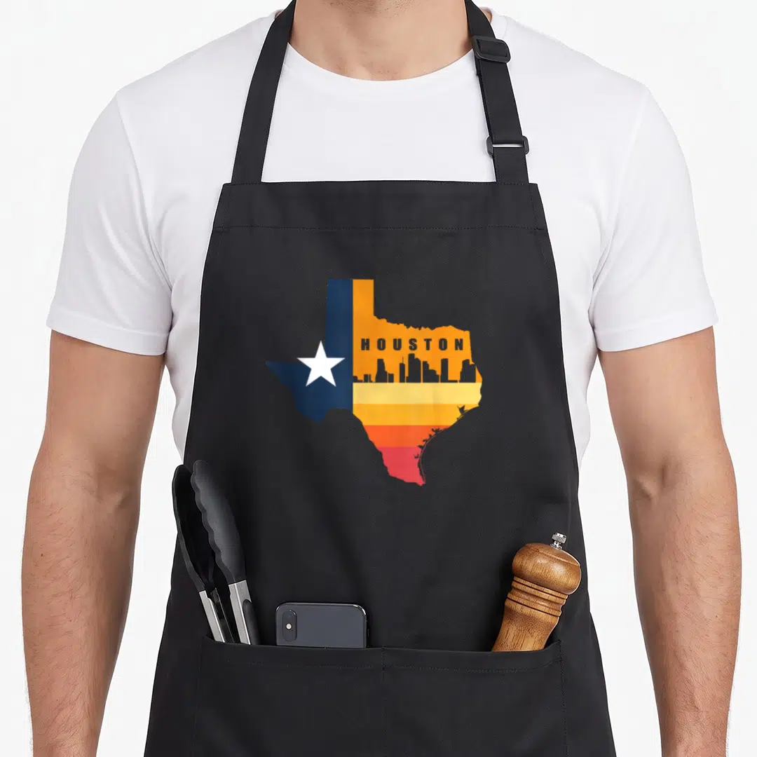 Houston texans apron - Texas map shape with HOUSTON text, grey skyline, white star, and orange yellow red stripes — shown on a black cotton canvas apron against a white background