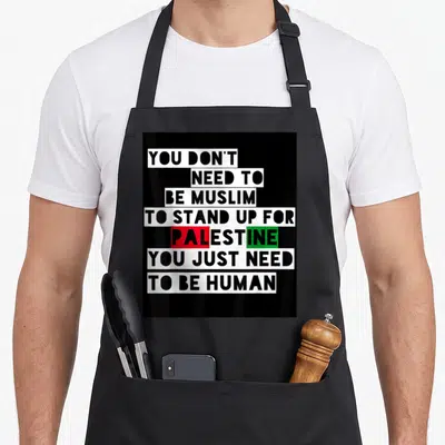 Cool free palestine apron - Stacked text blocks reading YOU DON'T NEED TO BE MUSLIM TO STAND UP FOR PALESTINE YOU JUST — shown on a black cotton canvas apron against a white background