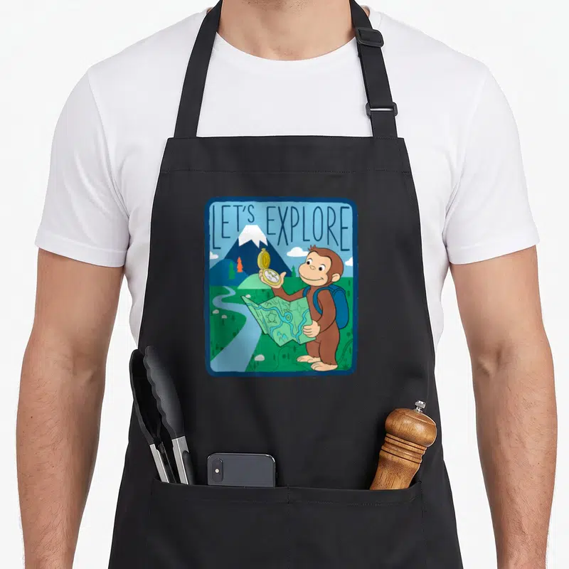 Curious outdoor apron - Cartoon monkey holding compass and map under LET'S EXPLORE text in blue-green-brown landscape — shown on a black cotton canvas apron against a white background