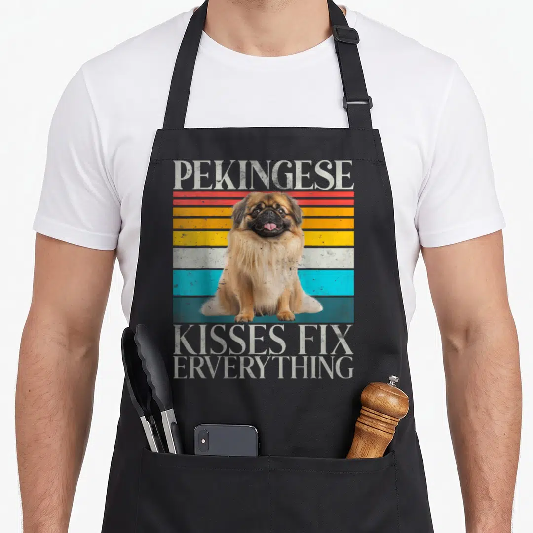 Kiss pekingese apron - Retro Pekingese dog illustration on red, yellow, white, and blue stripes with distressed text — shown on a black cotton canvas apron against a white background