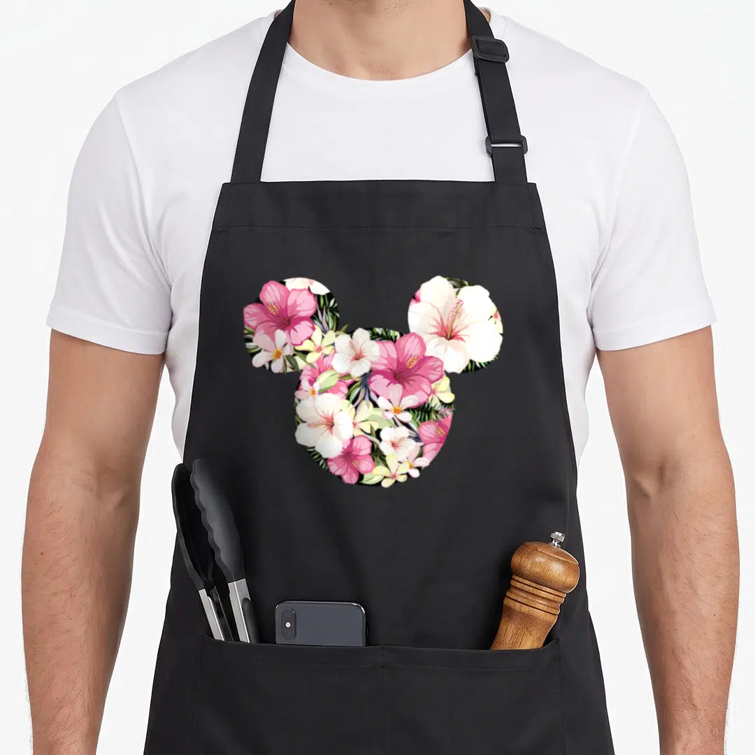 Silhouette tropical print aprons - Mickey head silhouette filled with pink white green and yellow hibiscus and plumeria — shown on a black cotton canvas apron against a white background