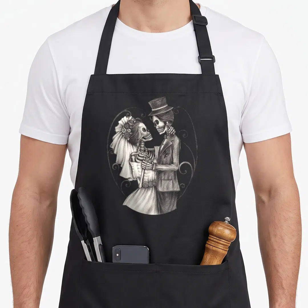 Dead wedding day aprons - Skeleton bride and groom holding hands inside a decorative heart frame in grey and white line — shown on a black cotton canvas apron against a white background