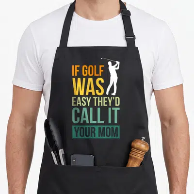 Theyd call golf apron - Stacked colorful text reading If Golf Was Easy They'd Call It Your Mom next to a white golfer — shown on a black cotton canvas apron against a white background