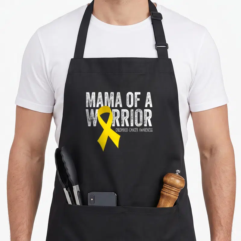 Childhood mama apron - MAMA OF A WARRIOR text with yellow ribbon forming the letter O for childhood cancer awareness — shown on a black cotton canvas apron against a white background