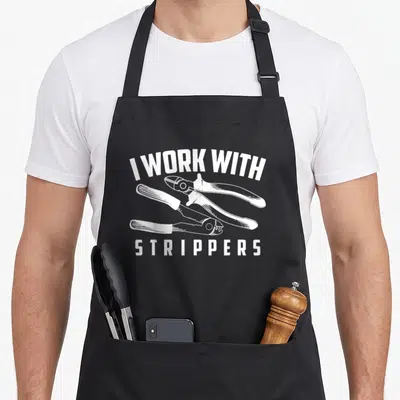 Stripper electrician humor apron - White I WORK WITH STRIPPERS text above three wire stripping tools — shown on a black cotton canvas apron against a white background