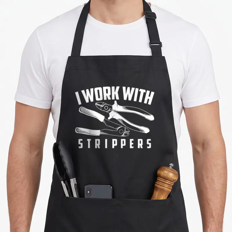 Stripper electrician humor apron - White I WORK WITH STRIPPERS text above three wire stripping tools — shown on a black cotton canvas apron against a white background