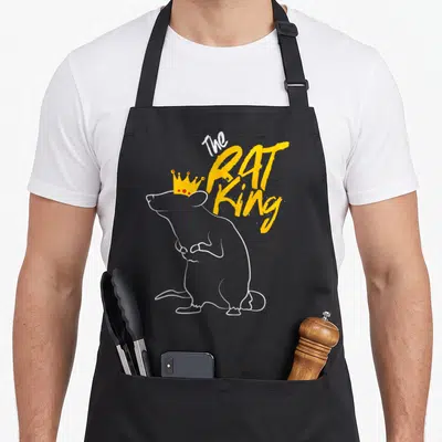 Rat nutcracker apron - White outline rat wearing yellow crown next to stacked orange text The Rat King — shown on a black cotton canvas apron against a white background