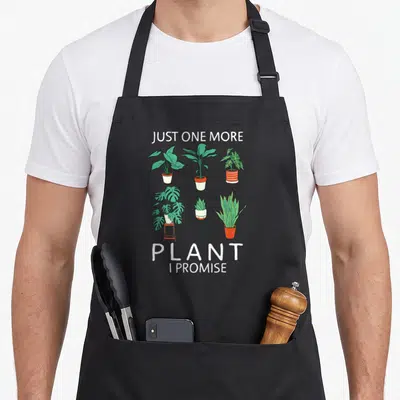 Promise plant apron - Six potted houseplants in cartoon style with text Just One More Plant I Promise — shown on a black cotton canvas apron against a white background
