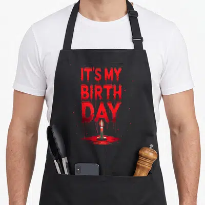 Bday birthday horror movie apron - Dripping red IT'S MY BIRTH DAY text above a green candle in a blood puddle — shown on a black cotton canvas apron against a white background