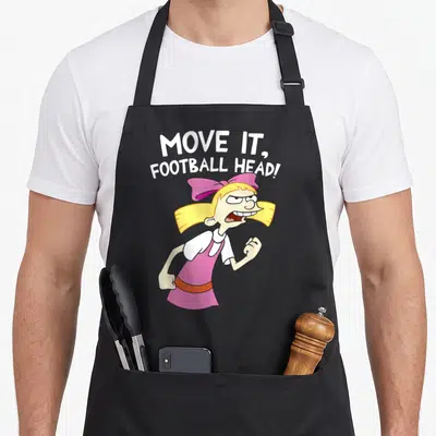 Hey football apron - Helga Pataki cartoon figure with arched MOVE IT FOOTBALL HEAD text in pink and yellow — shown on a black cotton canvas apron against a white background
